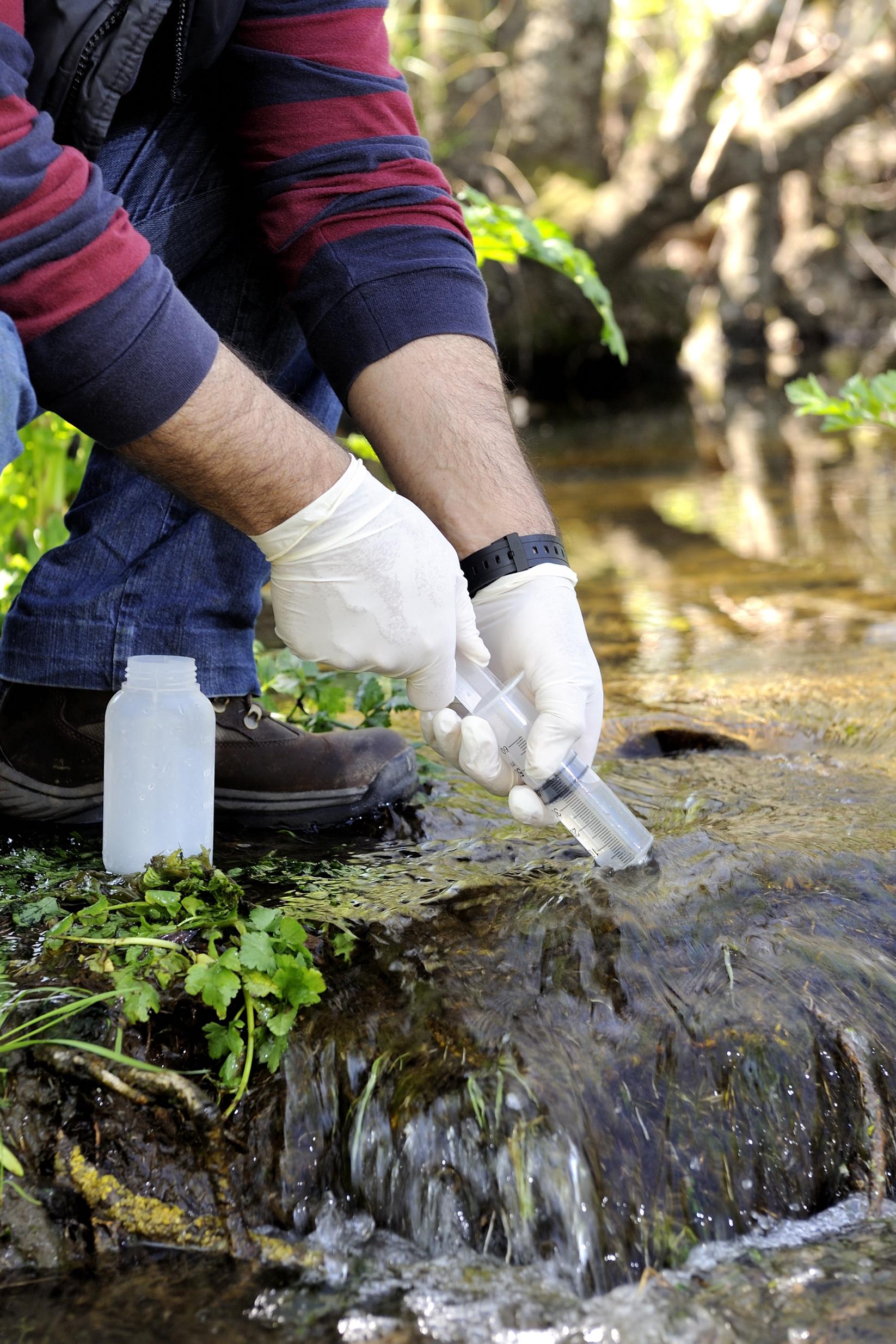 A technician collecting and testing a water sample from a clear Texas stream